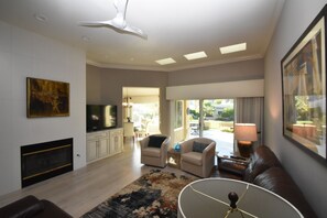 Amplia sala de estar con chimenea, televisor de pantalla plana, ventilador de techo y un ventanal que ofrece vistas al exterior.