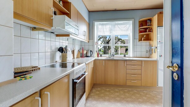 A kitchen with wooden cabinets, a built-in oven, a window with a view, and a blue door. - Stunning home in østermarie with WiFi (Østermarie)