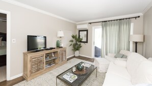 A living room with a TV, wooden cabinet, coffee table, white sofa, and a large window with curtains. - Downtown Charleston! Walking distance to The Battery! (Charleston)