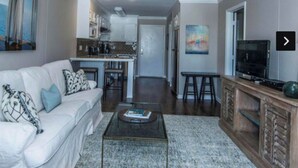 A living room with a white sofa, a coffee table, and a TV stand. There is a kitchen in the background with cabinets and a countertop. - Downtown Charleston! Walking distance to The Battery! (Charleston)