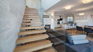 A modern interior with a wooden staircase, a glass railing, a dining area with chairs, and a kitchen in the background. - Cozy home in Kastel Gomilica with sauna (Kastel Gomilica)