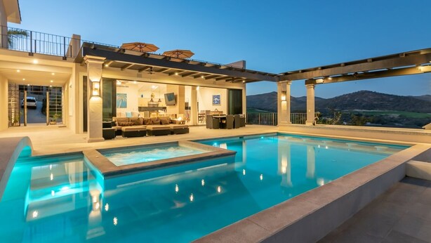 Ein moderner Poolbereich im Freien mit Sitzgelegenheiten und Blick auf die Berge.