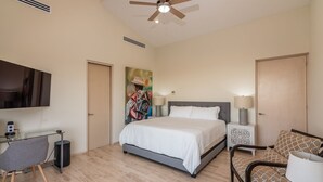 Ein Hotelzimmer mit Bett, Schreibtisch, Stuhl, Fernseher und Deckenventilator.