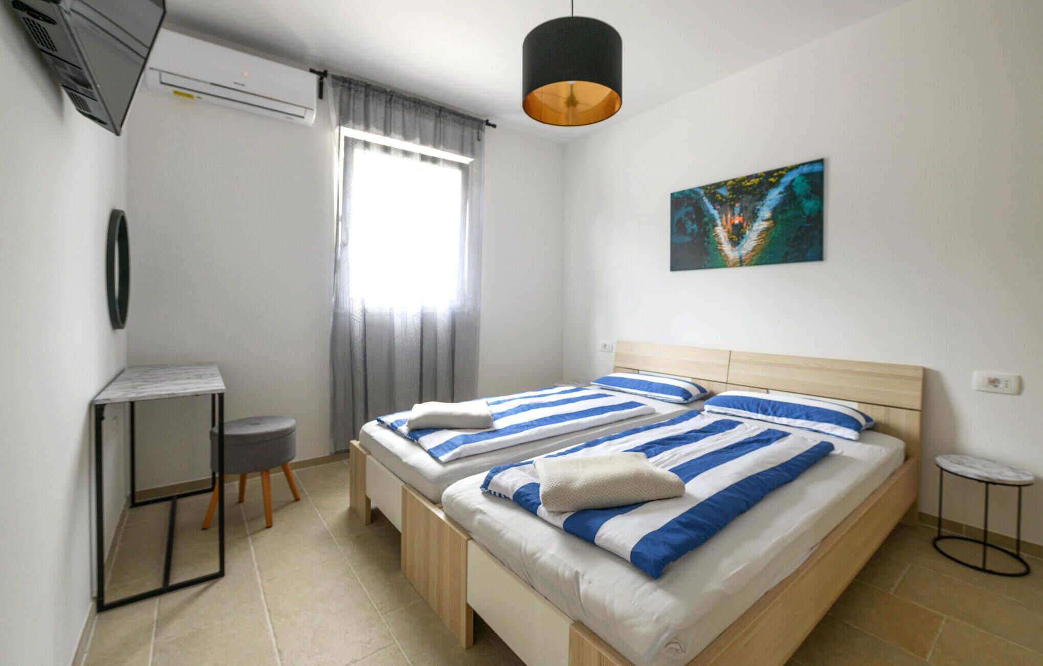 A bedroom with two beds, a desk, a chair, a small table, and a painting on the wall.
