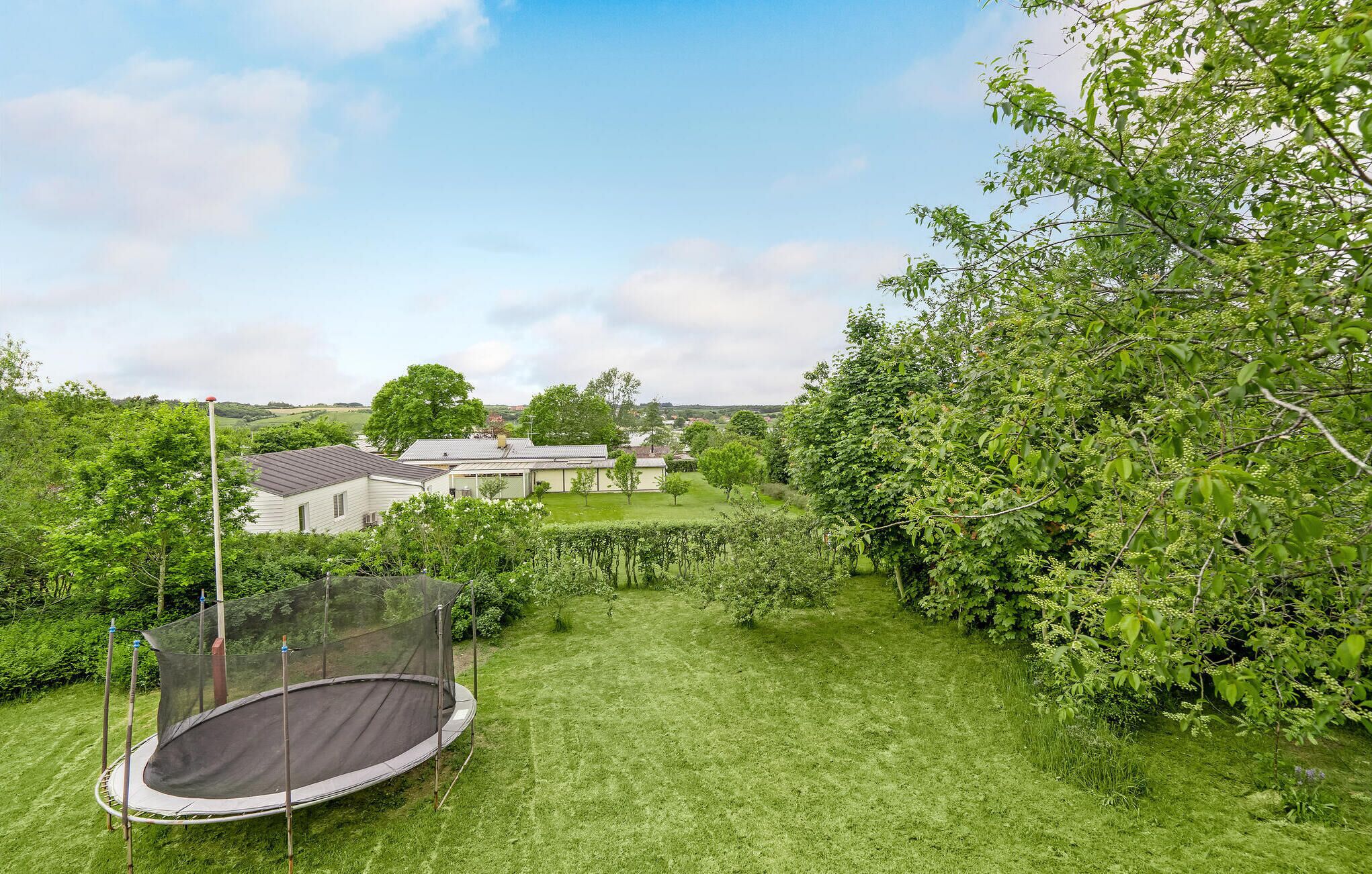 Ein Garten mit Trampolin, Haus und üppigem Grün.