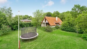 A house with a red roof, surrounded by lush greenery and a trampoline in the yard. - Nice home in Løgstrup with WiFi (Løgstrup)