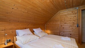 A wooden cabin room with a bed, bedside table, lamp, and a door. - 4 bedroom cozy home in Podstene (Podstene)