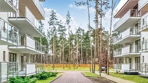Un immeuble d’appartements moderne dot é d’une cour intérieure, entouré de grands arbres et bordé d’une allée pavée.