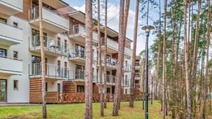 Un immeuble résidentiel à plusieurs étages, doté de balcons, entouré d’arbres et d’une zone herbeuse.