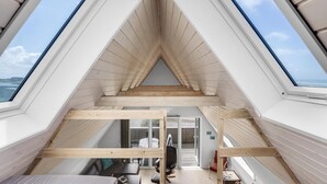 Une chambre moderne aménagée sous les combles, dotée de fenêtres de toit, de poutres en bois et offrant une vue sur la mer.