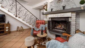 Una sala de estar acogedora con chimenea, un sillón de cuero rojo, una mesa de centro de madera y un televisor sobre un mueble de madera.