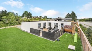 Una casa moderna con techo plano, patio cubierto y jardín cercado.
