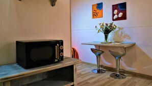 A compact kitchen with a microwave, a small table with a vase of flowers, and two bar stools.