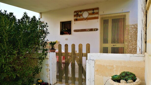 A house with a wooden gate, a small window with a plant, and a stone wall.