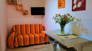 A living room with a striped orange sofa, a flat-screen TV, a table with a vase of flowers, and wall art.