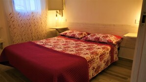 A bedroom with a bed, a nightstand, a wall-mounted lamp, and a window with a curtain.