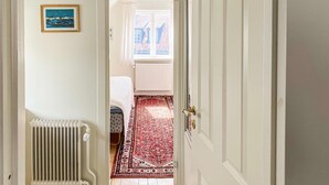 A narrow hallway with a radiator, a framed picture on the wall, and a view into a room with a bed and a patterned rug. - Lovely home in Visby with WiFi (Visby)