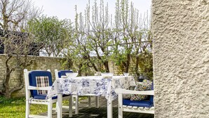 An outdoor dining area with a table set for two, surrounded by white chairs with blue cushions. - Lovely home in Visby with WiFi (Visby)