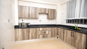 Een keuken met lichte houten kastjes, een zwart aanrecht en een raam met dunne gordijnen.