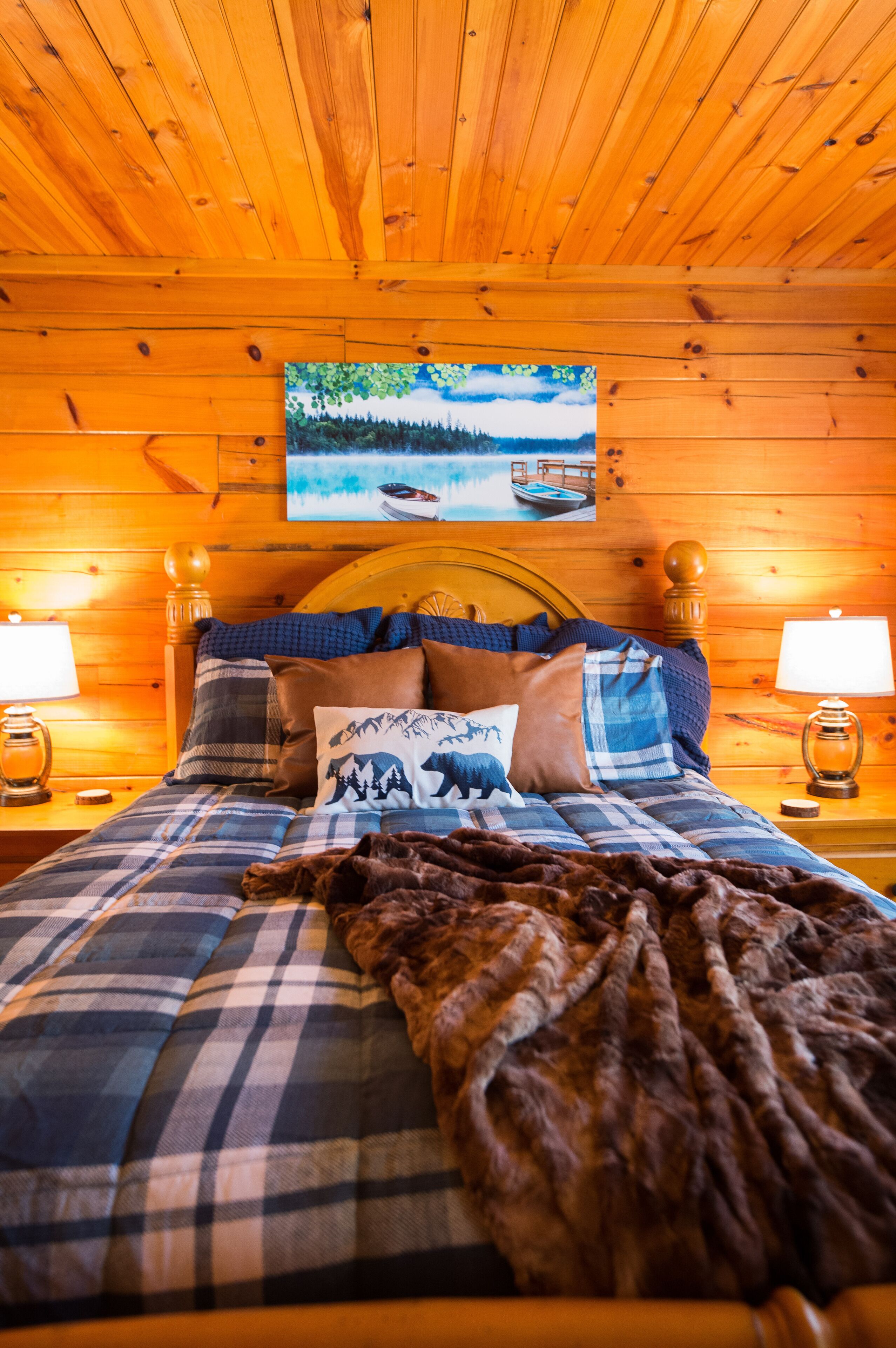 Une chambre dans une cabane en bois, avec un lit, des oreillers, une couverture et un tableau accroché au mur.
