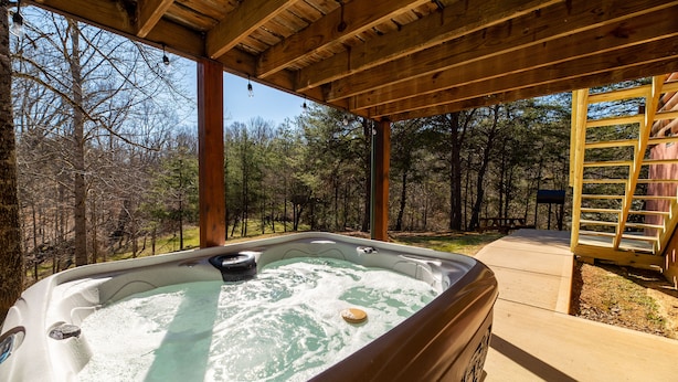 A hot tub in a wooden gazebo with a view of a forest.