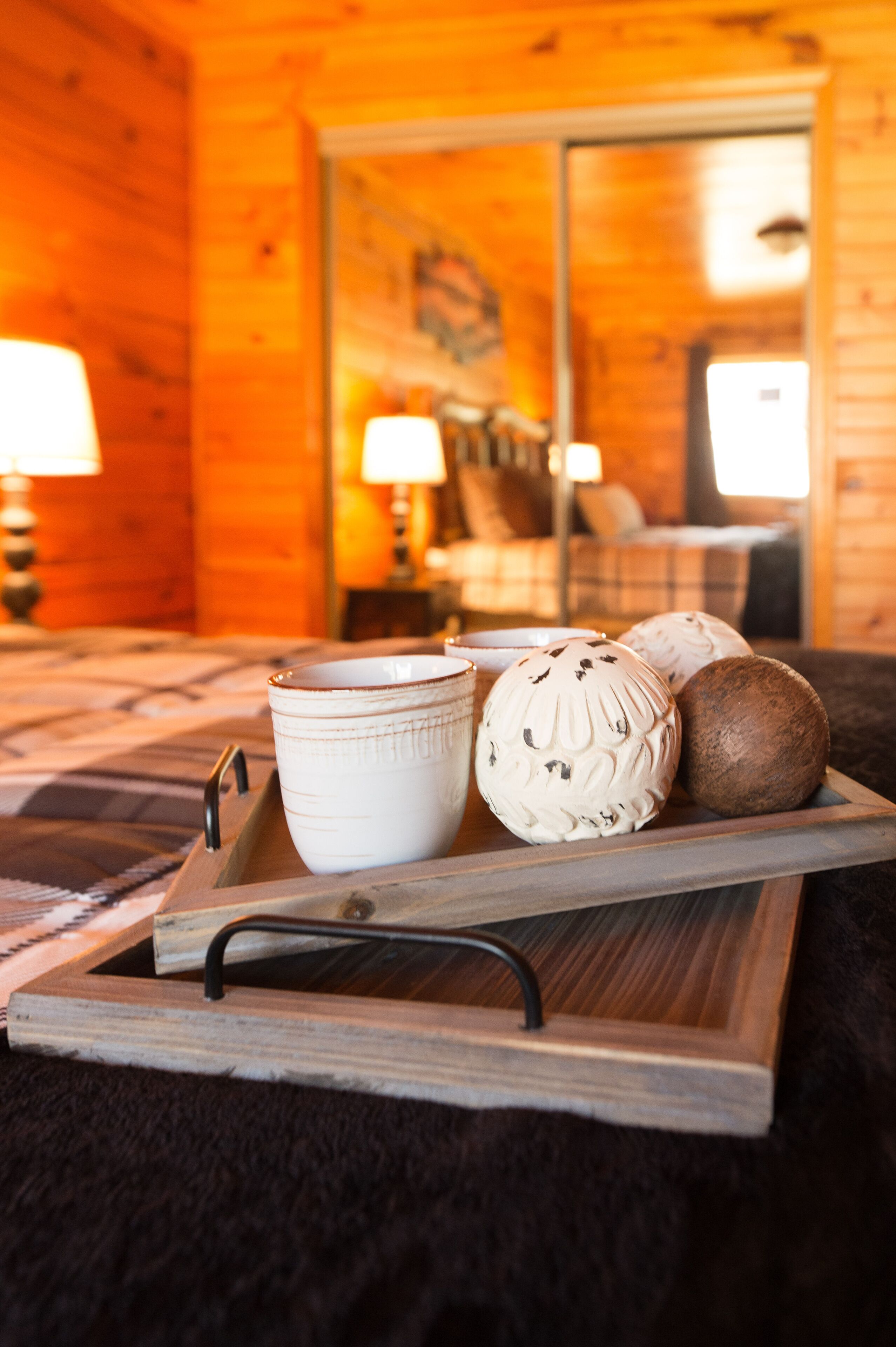 A wooden tray with a cup, a decorative bowl, and a coconut on a bed with a plaid blanket.