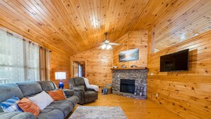 A log cabin interior with a sofa, armchair, fireplace, and television.