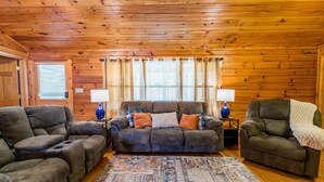A cozy living room with a wooden ceiling, two armchairs, a sofa, and a patterned rug.