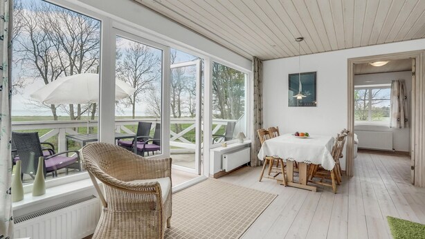 Ein heller, offener Wohnbereich mit großem Fenster zum Garten, einem Esstisch mit Stühlen und einem Korbstuhl im Vordergrund.