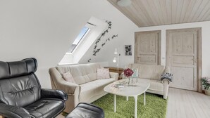 Ein modernes Wohnzimmer mit hohen Decken, einem Dachfenster, einem weißen Sofa, einem schwarzen Ledersessel und einem runden Couchtisch.