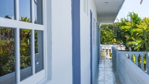 A long, narrow corridor with white walls and blue doors, leading to a covered area with a view of greenery. - Brisa Del Mar (Isla Holbox)