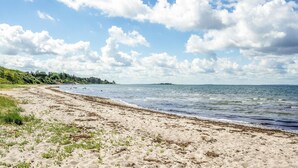 Une plage avec un rivage sablonneux, une mer calme et une île qui se profile à l’horizon.