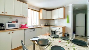 A compact kitchen with white cabinets, a microwave, a sink, and a dining table set with plates and glasses. - Awesome apartment in Torrevieja with WiFi (Torrevieja)