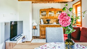 Una sala de estar con techo de madera, un televisor, una mesa con mantel floral y un jarrón con flores rosas.