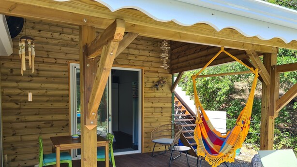 Une cabane en bois avec une véranda, un hamac et un paillasson.