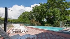 Una piscina con bordo piastrellato, circondata da alberi e un cielo sereno.