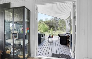 Een modern terras buiten, met aan één kant een glazen omheining, en een helder uitzicht op de omliggende groene omgeving. Het houten terras is goed onderhouden.