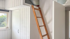 Una habitación con paredes blancas empapeladas, una escalera de madera, un ventanal y una puerta.