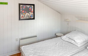 A room with a bed, a small table, a wall-mounted lamp, and a painting.