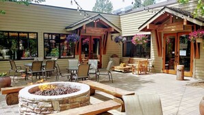 An outdoor patio with stone fire pit, wooden benches, and tables. There are hanging flower baskets and a sign for 'The Outfitters'. - Best Location and layout at 7th Mountain 1024 SF 2 Bed/2 Bath - Pet Friendly (Bend)