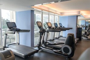 Een fitnessruimte met loopbanden en trainingsapparatuur, grote ramen en uitzicht over de stad.