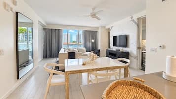 A modern hotel room with a dining area, a flat-screen TV, and a view of the city.