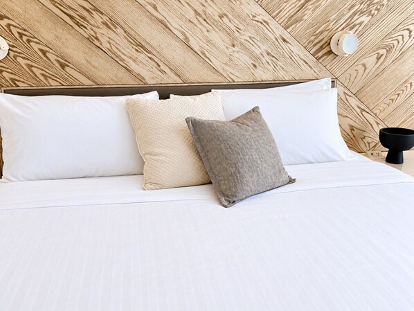 A neatly made bed with white linens and two pillows, one beige and one gray, against a wooden headboard.
