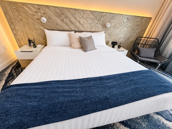 Een hotelkamer met een groot bed, een houten hoofdbord, een nachtkastje met een lamp en een stoel met een kussen.
