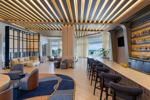 A modern hotel lobby with a bar area, seating arrangements, and a view of the ocean.