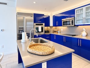 A modern kitchen with blue cabinets, stainless steel appliances, and a central island with a woven basket.