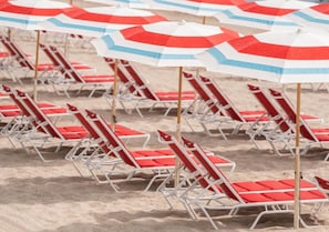 Rijen strandstoelen en parasols op een zandstrand.