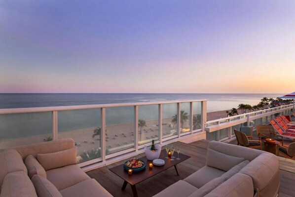 A balcony with a view of the beach and ocean, furnished with sofas and a table with drinks.