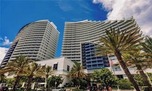 Een modern hotel met een gebogen gevel, diverse balkons en palmbomen op de voorgrond.