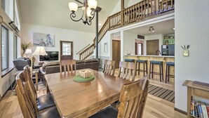 A spacious dining area with a wooden table and chairs, a chandelier, and a staircase leading to an upper level. - 'The River Home' Cabin w/ Yard: Near Wolf Creek! (Pagosa Springs)